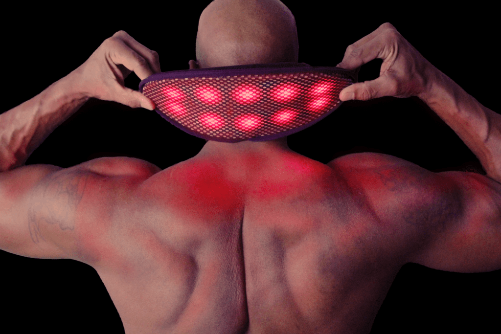 A person treating their upper back with a red light therapy device.